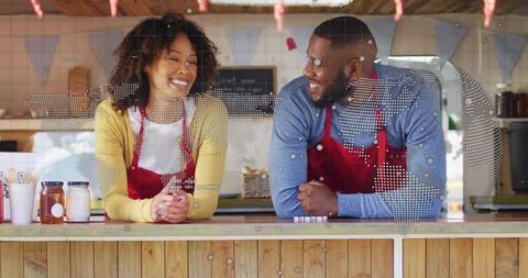 Smiling Cafe Staff Leaning on Wooden Counter Wearing Red Aprons with World Map Overlay
