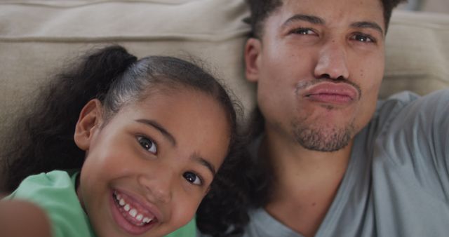 Happy biracial father and daughter sitting on sofa taking selfies - Download Free Stock Photos Pikwizard.com