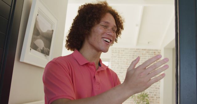 Image of happy biracial young man opening door and welcoming someone. Domestic life and spending time at home.