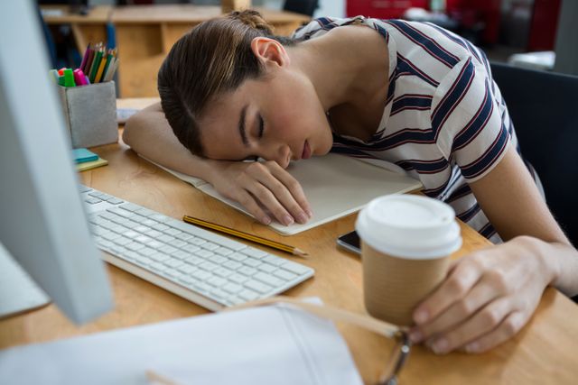 This image depicts an overworked graphic designer sleeping at their desk in a creative office. It can be used to illustrate concepts related to workplace stress, burnout, and the importance of work-life balance. Ideal for articles, blogs, and presentations on employee well-being, productivity, and office culture.