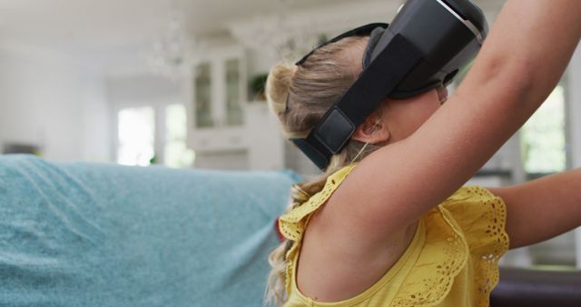 Happy caucasian girl at home, sitting on couch wearing vr headset and smiling. happy family, free time at home.