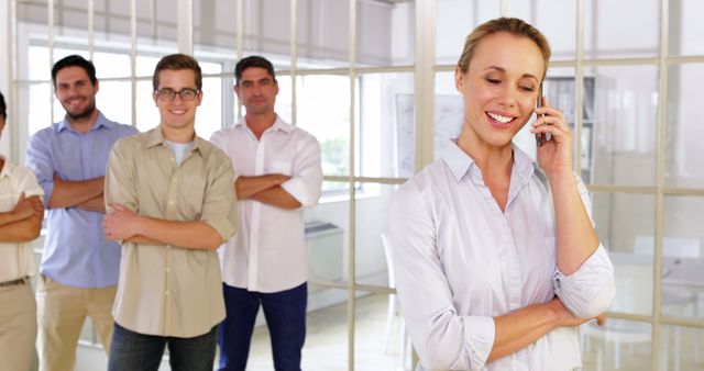 Confident Businesswoman Talking on Phone with Colleagues in Background - Download Free Stock Images Pikwizard.com