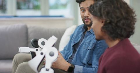 Young men discussing white robotic arm components on sofa in casual hobby prototyping