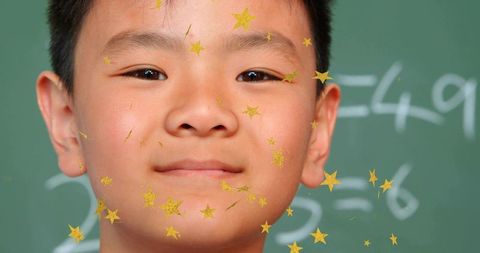 Smiling chinese schoolboy wearing gold star stickers on cheeks with chalkboard math