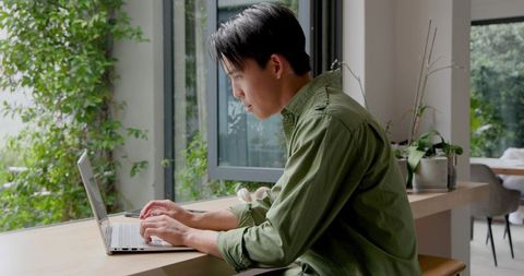 Asian Man Working on Laptop in Modern Office with Natural Light