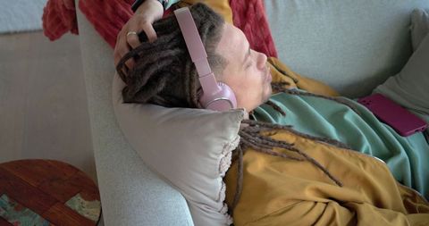African american man relaxing with pink headphones and smartphone on couch