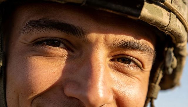 Smiling soldier looking at camera wearing camouflage helmet chinstrap sunlit close-up portrait