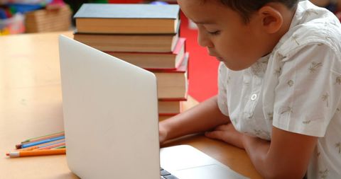 Young schoolboy studying with laptop in classroom