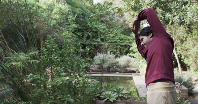Man performing stretching exercises in a lush green garden. Ideal for topics related to fitness, wellness, outdoor activities, gardening, and promoting a healthy lifestyle.