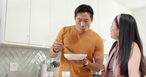 Couple tasting homemade meal in bright modern kitchen sharing casual cooking moment