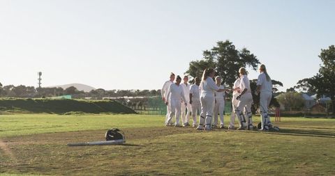 Female cricket team huddling after match on sunny pitch