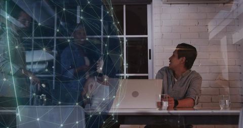 Asian man working on laptop during team meeting with holographic network globe overlay