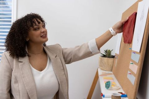 Woman arranging red fabric sample on corkboard mood board in minimalist design studio
