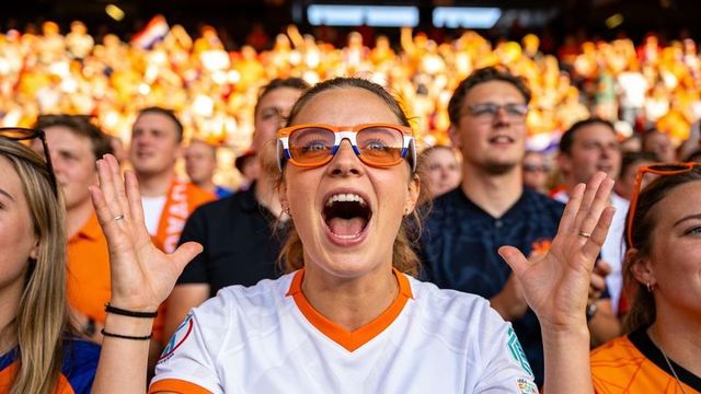 Passionate fan cheering in stadium wearing orange sunglasses and white jersey, vibrant crowd