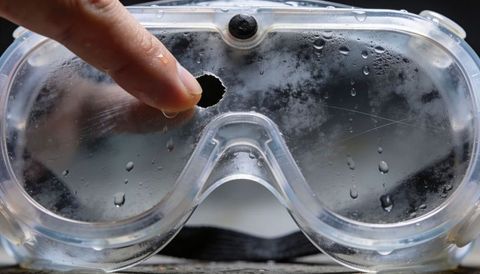 Punctured safety goggles closeup showing hole, condensation and scratches for ppe safety