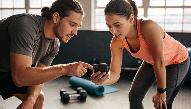 Trainer guiding client with smartphone while checking workout progress in gym session