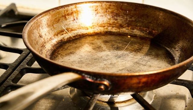 Well-used riveted skillet showing darkened patina and scratches on gas stove