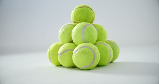 Bright neon green tennis balls arranged in a pyramid against a white background. Ideal for promoting sports and fitness products, tennis gear, or minimalist-themed designs. Can be used in advertisements, social media posts, or sports-related editorial content.