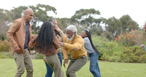 Multigenerational family playing on park lawn, grandparent reaching toward laughing child