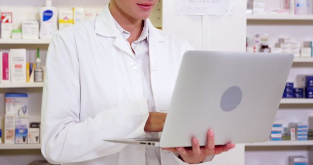 Pharmacist standing at counter and using laptop in pharmacy