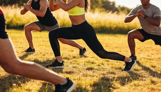 Group outdoor fitness class performing lunges at golden hour in meadow park