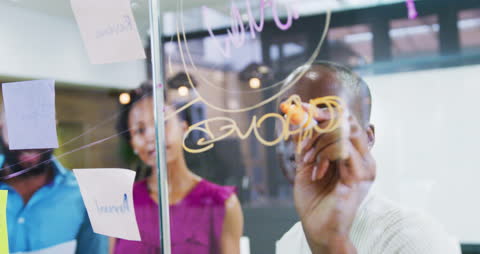 Diverse Team Collaborating and Taking Notes on Glass Wall