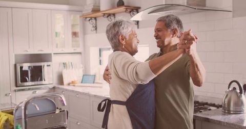 Senior couple dancing in sunlit kitchen sharing joyful moment and warm cozy companionship