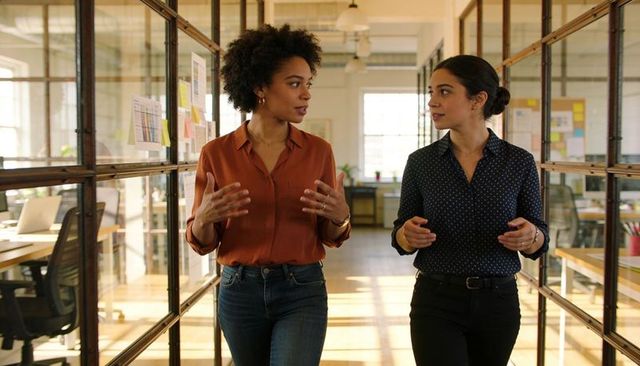 Two colleagues walking and discussing in modern open-plan office corridor