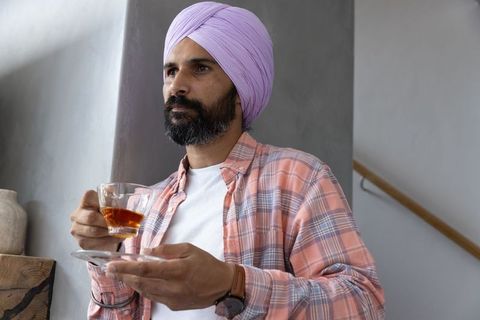 Elegant man with lavender turban enjoying tea indoors