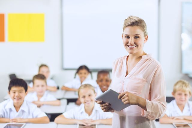 Smiling teacher using digital tablet in classroom with students. Ideal for educational content, technology in education, school brochures, and teacher training materials.