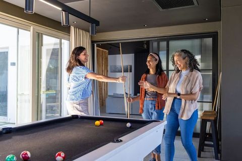 Diverse women playing pool in modern home game room laughing and socializing casual gathering
