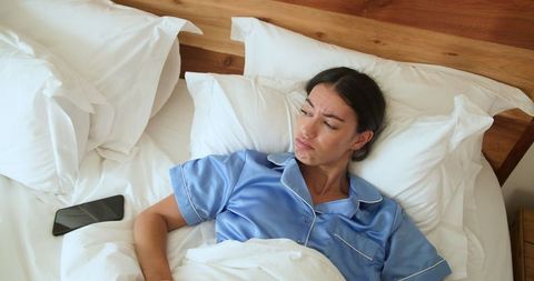 Woman in Blue Pajamas Resting on Bed with Smartphone Nearby