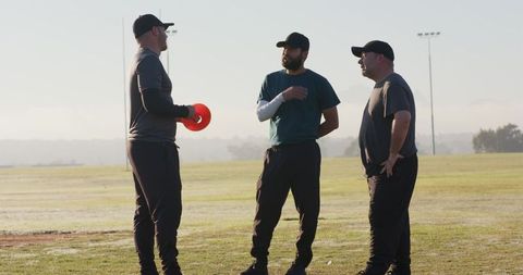 Coaches discussing strategy on morning sports field holding orange training marker disc