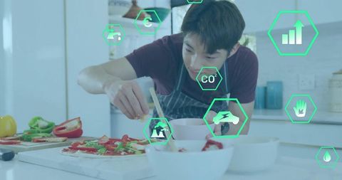 Korean teenager sprinkling pizza toppings wearing striped apron in modern kitchen with ar icons