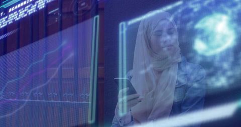 Young woman wearing hijab holding smartphone with holographic interface in blue overlay