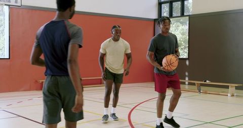 African american men practicing basketball drill with coach signaling play in gym
