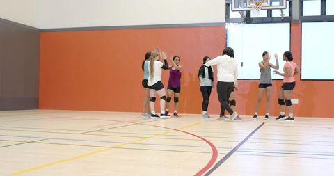 Diverse women's basketball team celebrating with courtside high-fives near hoop