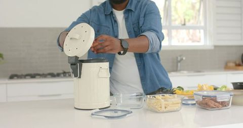 African man lifting lid on cream compost bin, organizing containers in bright kitchen