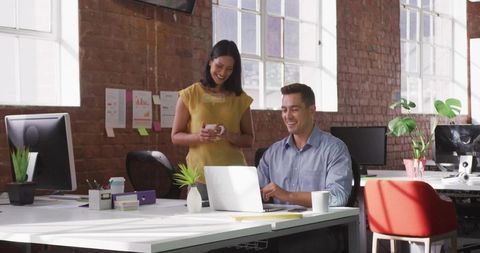 Business Colleagues Collaborating in Bright Open-Plan Office with Laptop, Coffee, Plants