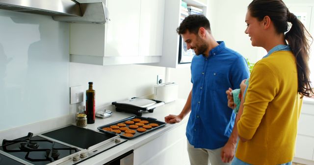 Couple enjoys baking muffins together in their modern kitchen. They are smiling and appear relaxed, suggesting a joyful and cooperative domestic life. The scene represents family bonding, home cooking, and teamwork, making it suitable for advertisements related to kitchen appliances, family life, or culinary activities.