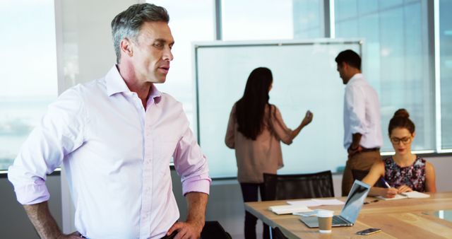 Business team collaborating in modern office with whiteboard and technology. Image shows professional adults discussing and brainstorming ideas during a business meeting. Useful for themes related to teamwork, corporate environment, business planning, and office productivity.