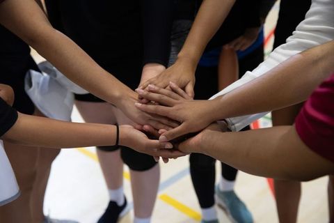 Youth Team Huddling with Stacked Hands on Indoor Court Showing Unity and Diversity