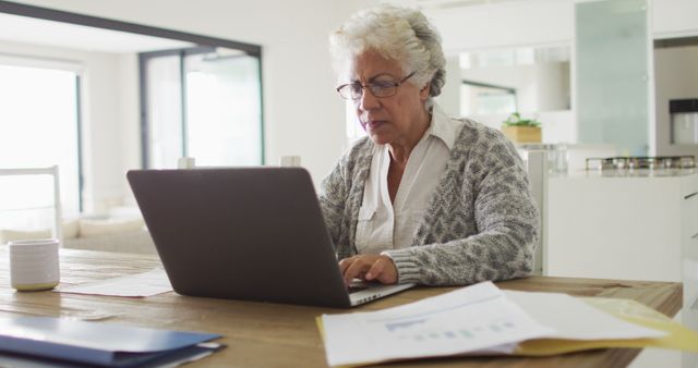 Senior woman using laptop at home office, focused on work. Great for illustrating remote work, elderly technology usage, senior professionals, and home office setups. Perfect for articles on aging in the workplace, retirement activities, staying productive, and senior employment.