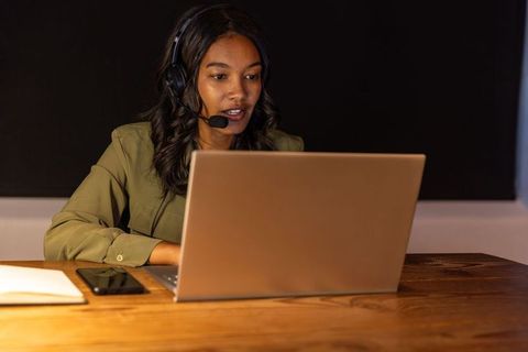 African american woman speaking on headset while typing on laptop in modern workspace