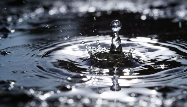 Silver water droplet crown with radiating ripples macro close-up capturing fluid motion