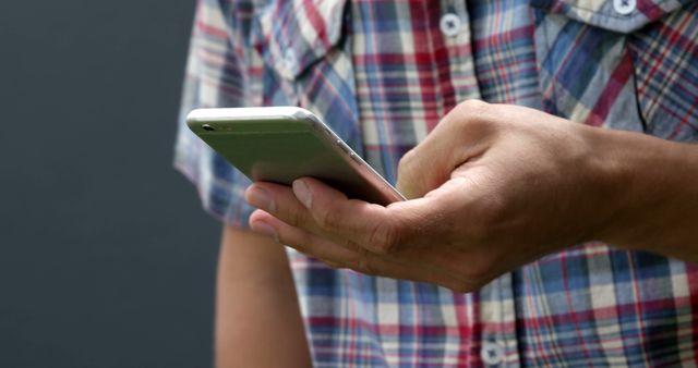 Close-up of person using smartphone, dressed in casual plaid shirt. Perfect for illustrating mobile communication, modern technology use, or promoting apps and gadgets.