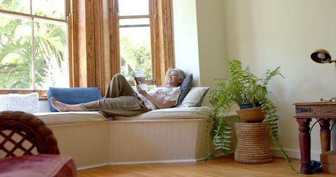 Senior Woman Relaxing in Cozy Window Seat Reading Book