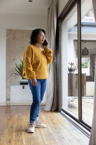 Senior asian woman talking on smartphone by glass door