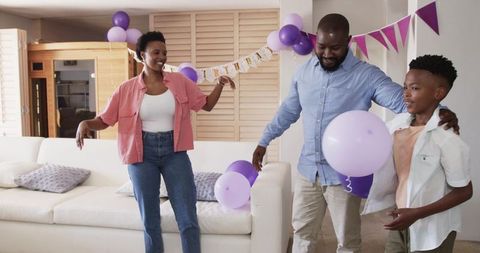 African American Family Celebrating at Home with Purple Balloons, Bunting, Smiling Parents