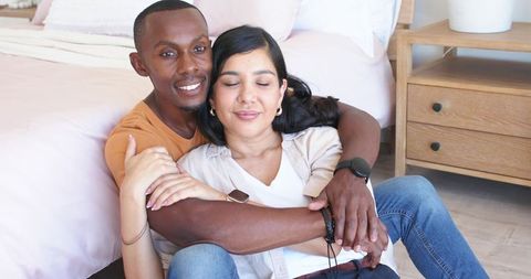 Cuddling couple wearing smartwatches relaxing on bedroom floor by wooden nightstand